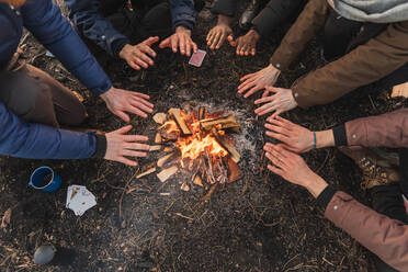 Von oben auf der Ernte multiethnische Freunde halten sich über einem brennenden Lagerfeuer an den Händen, während sie Zeit in der Natur verbringen - ADSF26398