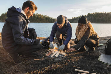 Männer und Frauen in Oberbekleidung und Handschuhen legen Feuerholz für das Lagerfeuer, während sie Zeit in der Natur verbringen - ADSF26401