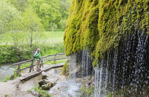 Älterer Wanderer bewundert den Wasserfall in den Dreimühlen, der einen moosbewachsenen Hang hinunterstürzt - GWF07093