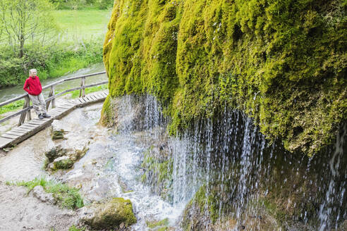 Wanderin bewundert Dreimuhlen-Wasserfall, der einen moosbewachsenen Hang hinunterstürzt - GWF07095