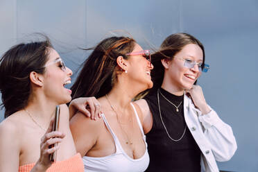 Positive Freundinnen mit trendigen Sonnenbrillen und lässiger Kleidung, die fröhlich lachen und eine angenehme Zeit miteinander verbringen - ADSF26428