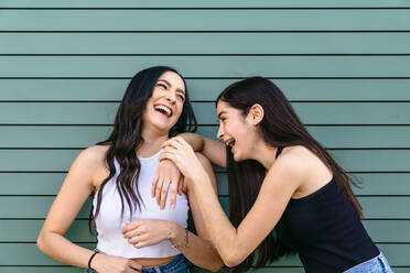 Positive female teen leaning on shoulder of sibling while having fun on green background in daytime - ADSF26436