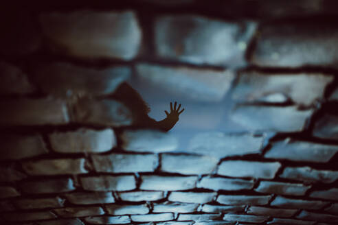 High angle of reflection on wet cobblestone ground of unrecognizable person reaching hand with stop gesture - ADSF26450