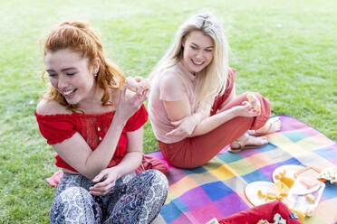 Smiling female friends having doughnut while sitting on picnic blanket - WPEF05045