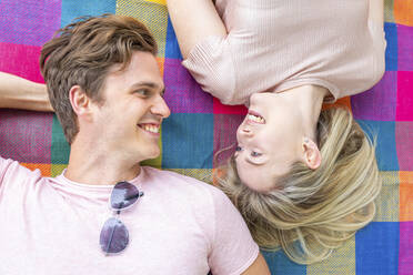 Smiling couple lying face to face on picnic blanket - WPEF05047