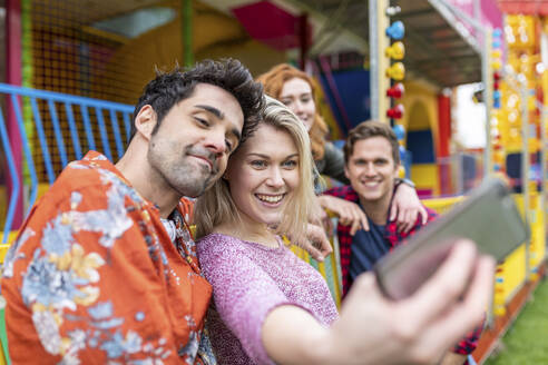Lächelnde Frau nimmt Selfie mit Freunden durch Smartphone im Vergnügungspark - WPEF05056