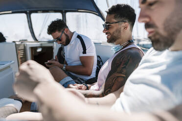 Mann benutzt Mobiltelefon mit männlichen Freunden auf einer Jacht an einem sonnigen Tag - EGAF02427