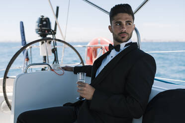 Young man with drink looking away while traveling in yacht during vacation - EGAF02435