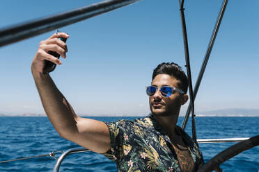 Junger Mann nimmt Selfie durch Smartphone in Yacht auf sonnigen Tag - EGAF02441