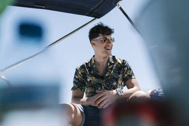 Young man laughing while sitting in yacht during sunny day - EGAF02456