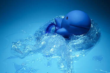 Arrangement eines blauen Spielzeugdelfins, der in Plastikmüll eingewickelt ist, der die Umweltprobleme der Ozeane darstellt - ADSF26512