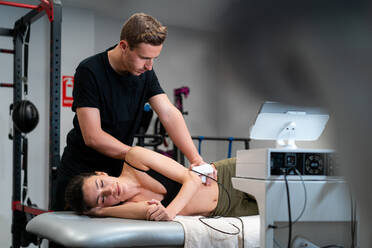 Männlicher Physiotherapeut bei der Anwendung eines Lasers auf die Rückenhaut einer Frau während einer medizinischen Behandlung im Krankenhaus - ADSF26515