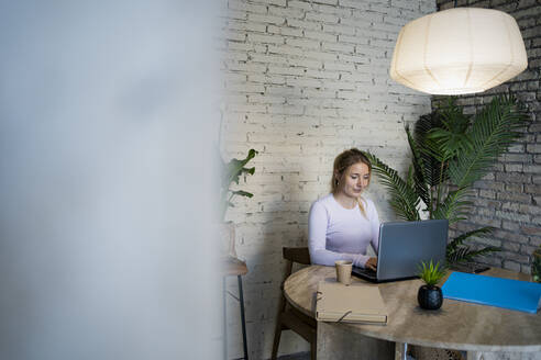 Junge Freiberuflerin mit Laptop bei der Arbeit zu Hause - RCPF01177