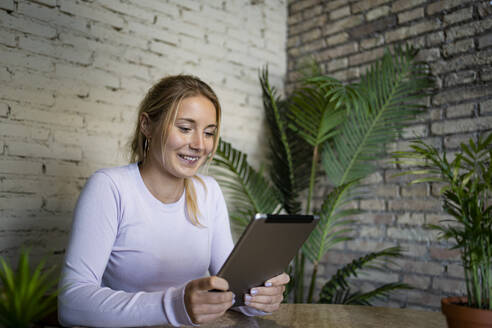 Lächelnde junge Geschäftsfrau, die zu Hause ein digitales Tablet benutzt - RCPF01181