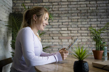 Lächelnde blonde Freiberuflerin bei der Arbeit an einem digitalen Tablet zu Hause - RCPF01182