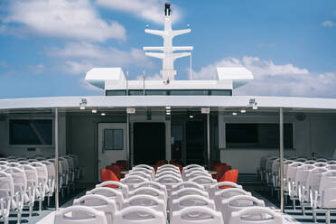 Deck of cruise boat with empty white chairs in row under clear sky with clouds - ADSF26533