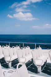 Empty white chairs on deck of cruise boat sailing in blue sea water - ADSF26534