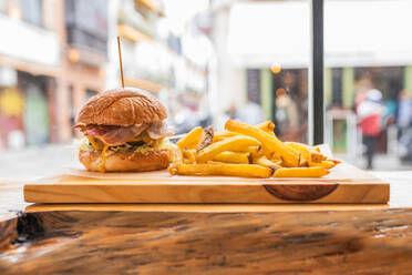 Leckerer frischer Hamburger und knusprige Pommes frites, serviert auf einem Holzbrett in einem modernen Fastfood-Restaurant - ADSF26553