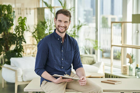 Happy male professional with digital tablet sitting on table at home - AKLF00315