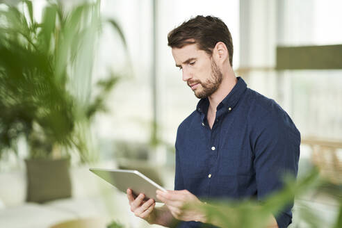 Männlicher Berufstätiger, der ein digitales Tablet bei der Arbeit von zu Hause aus benutzt - AKLF00317