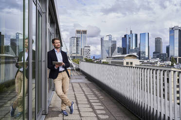 Businessman looking away while holding digital tablet on rooftop - AKLF00342