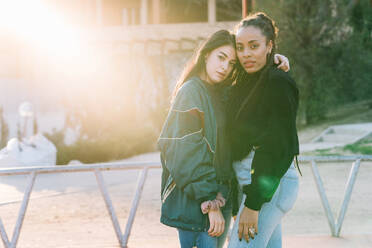 Diverse lesbian girlfriends in trendy wear embracing and looking at camera on walkway - ADSF26565