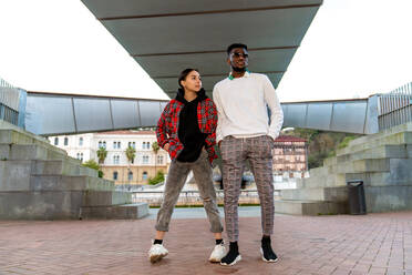 Trendy African American male standing with ethnic female beloved with hand in pocket on urban pavement - ADSF26609