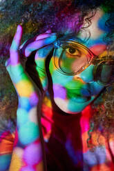Porträt einer attraktiven jungen Afroamerikanerin mit modischer Sonnenbrille, die in die Kamera schaut, während sie in Neonlichtern steht - ADSF26632