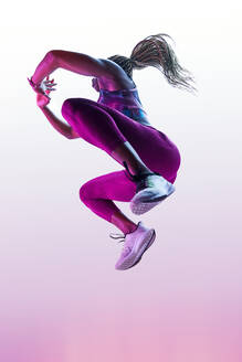 Anonyme afroamerikanische Sportlerin mit fliegenden Haaren in Sportkleidung, die beim Training mit gefalteten Händen springt - ADSF26643