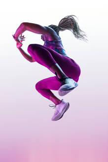 Anonymous African American female athlete with flying hair in sports clothes jumping with clasped hands during training - ADSF26643