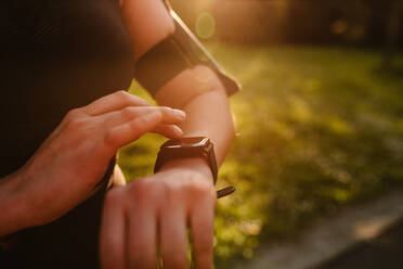 Crop anonymous female athlete watching pulse rate on wearable bracelet display during workout in sunlight - ADSF26661