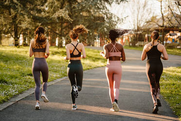 Rückenansicht multirassische Läuferinnen in Sportkleidung beim Joggen während des Ausdauertrainings auf einem Gehweg in der Stadt - ADSF26662