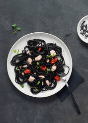 Von oben schwarze Tinte Spaghetti mit Lachs in Keramikteller auf dunklem Hintergrund - ADSF26677