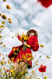 Von unten elegante Frau mit Hut inmitten blühender Blumen auf einem Feld auf dem Lande an einem Sommertag - ADSF26694