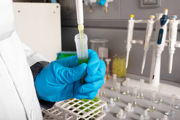 Anonymer Chemiker gießt Marihuanaöl aus einer Pipette in ein Probenröhrchen während einer Untersuchung im Labor - ADSF26734