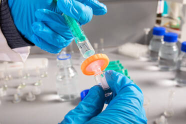 Crop unrecognizable biologist in latex gloves filling injector with liquid from small bottle in laboratory - ADSF26735