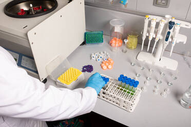 From above of crop unrecognizable scientist with sample tubes in rack against centrifugal machine in cannabis laboratory - ADSF26737