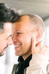 Seitenansicht des glücklichen jungen multirassischen homosexuellen Paares, das sich auf der Straße an einem sonnigen Tag umarmt und gegenseitig anschaut - ADSF26767