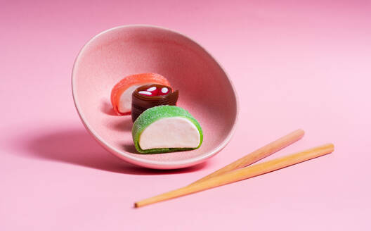 Appetizing colorful sweet sushi served on ceramic plate with wooden chopsticks placed on pink background - ADSF26772