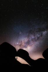 Silhouette eines anonymen Touristen, der auf einer Klippe steht und die am Nachthimmel leuchtenden Sterne bewundert - ADSF26788