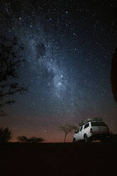 Low angle of off road vehicle parked in nature among trees under glowing stars at night - ADSF26789