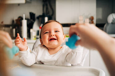 Nettes lachendes Baby in weißem Hemd sitzt in Baby-Fütterung Stuhl in der modernen Küche - ADSF26804