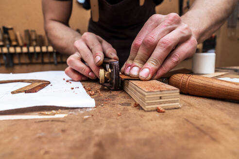 Unbekannter Handwerker schneidet Holzstück mit Tischler auf Tisch mit Papierbogen in Werkstatt - ADSF26931