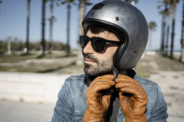 Gut aussehender Mann mit Handschuh beim Einstellen des Helms an einem sonnigen Tag - RCPF01198