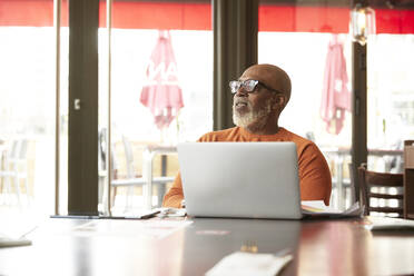 Businessman looking away while sitting with laptop in restaurant - PMF02029