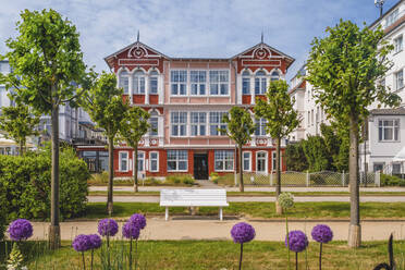 Germany, Mecklenburg-Western Pomerania, Heringsdorf, Flowers blooming in front of empty park bench with hotel in background - KEBF01998