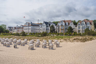 Deutschland, Mecklenburg-Vorpommern, Heringsdorf, Strandkörbe mit Kapuze am Sandstrand mit Wohnhäusern im Hintergrund - KEBF01999