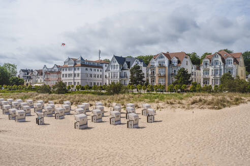 Deutschland, Mecklenburg-Vorpommern, Heringsdorf, Strandkörbe mit Kapuze am Sandstrand mit Wohnhäusern im Hintergrund - KEBF01999