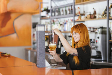 Lächelnde rothaarige Kellnerin füllt ein Bierglas aus dem Zapfhahn an der Bar - LJF02243