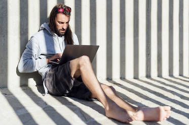 Junger männlicher Freiberufler mit Laptop an einem sonnigen Tag - PGF00666